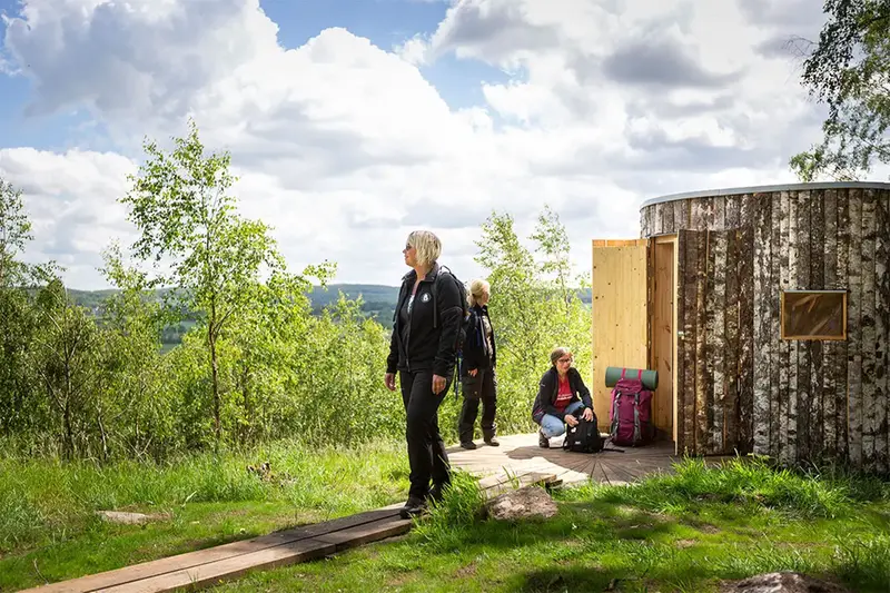 Tre kvinnor framför ett av de arkitektritade vindskydden på Hovdala naturområde och Vandringscentrum