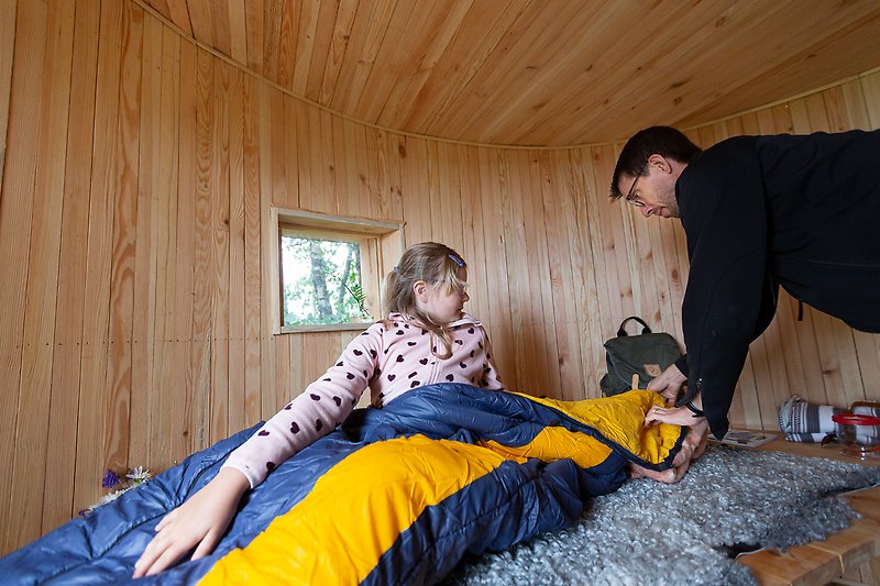 En man och en flicka förbereder nattplatsen i ett vindskydd med sovsäck och ullskinn som underlag.